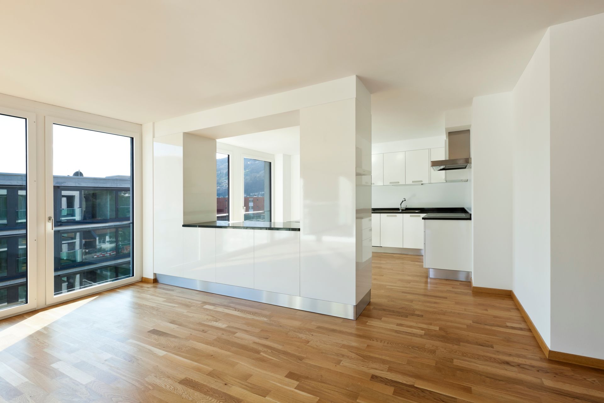 Appartement lumineux et vide avec parquet, grandes fenêtres et cuisine ouverte.