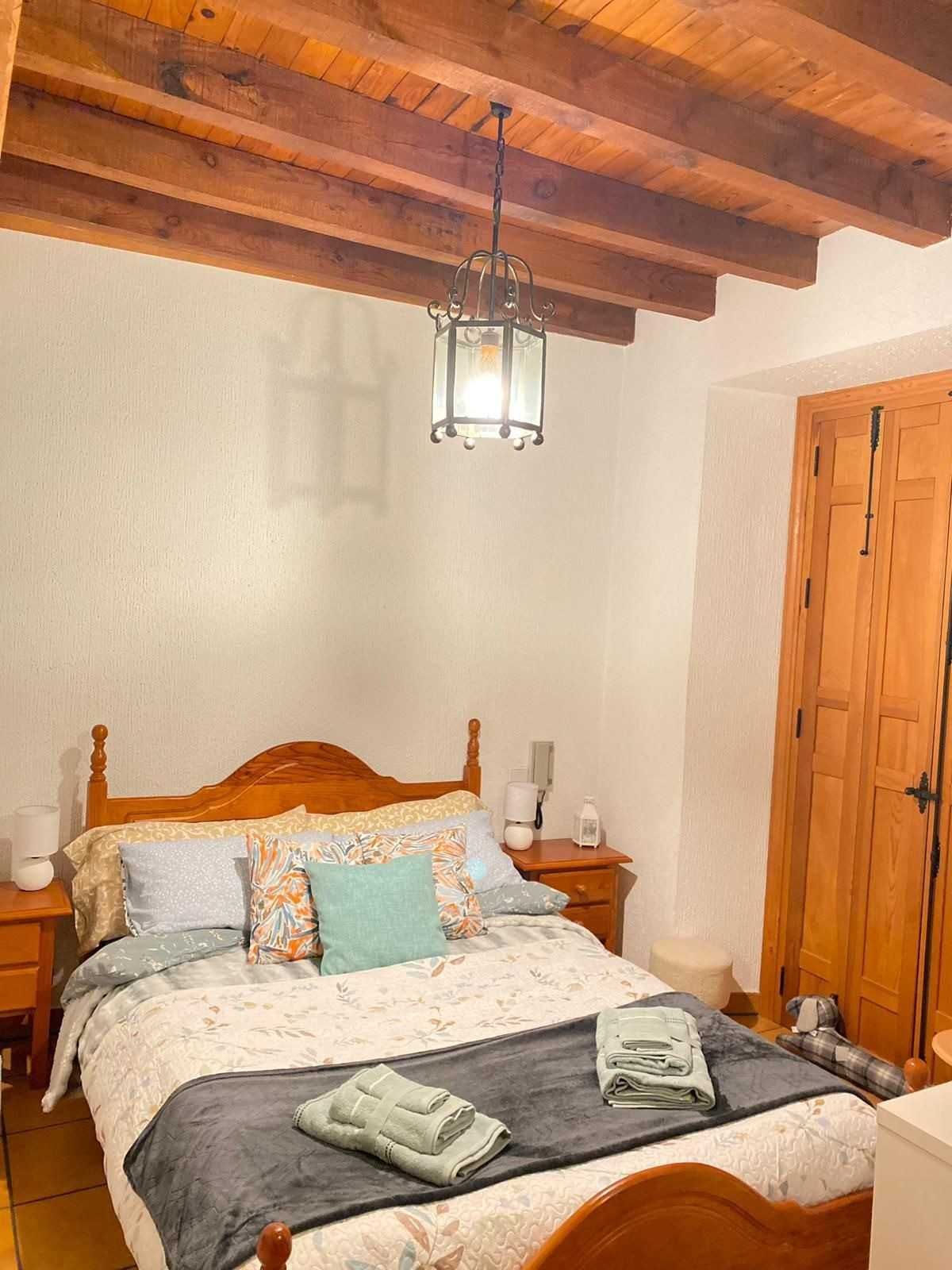 Acogedora habitación con techo de vigas de madera, farol colgante, cama de madera y armario.