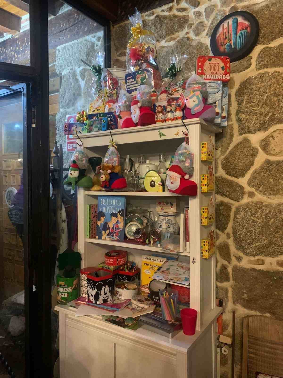 Estantería blanca decorada con coloridas figuritas y adornos navideños contra una pared de piedra.
