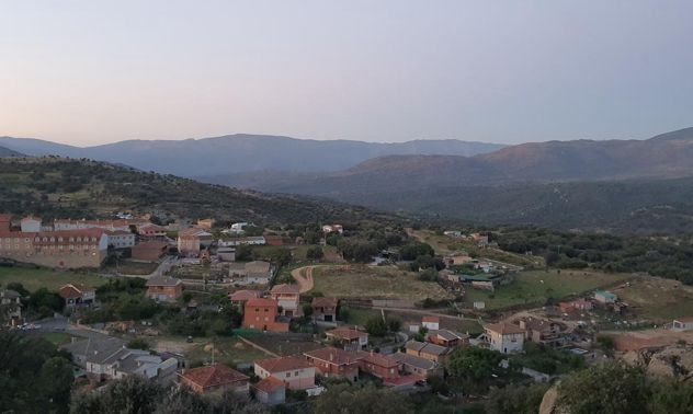 Pueblo con casas de tejados rojos en un valle verde bajo montañas brumosas al atardecer.