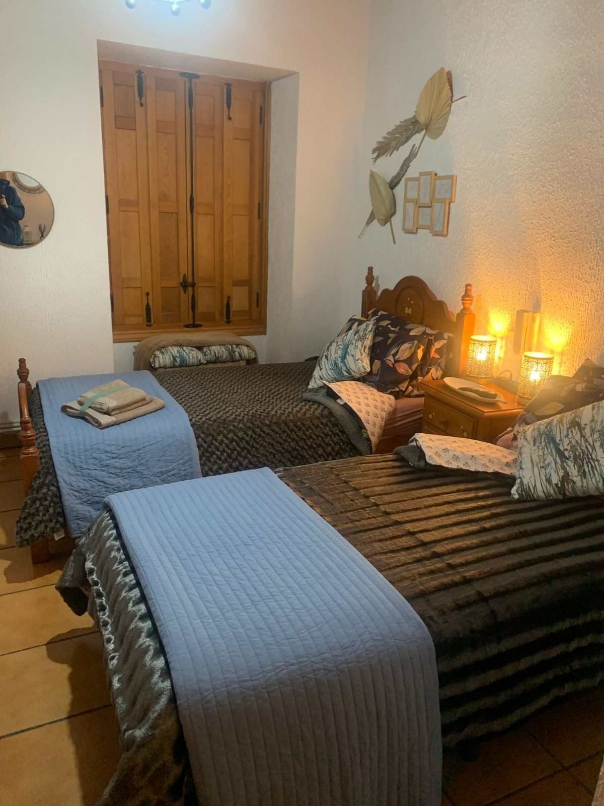 Acogedora habitación con dos camas individuales, ropa de cama azul y marrón, puertas de armario de madera y una cálida iluminación con lámpara de noche.