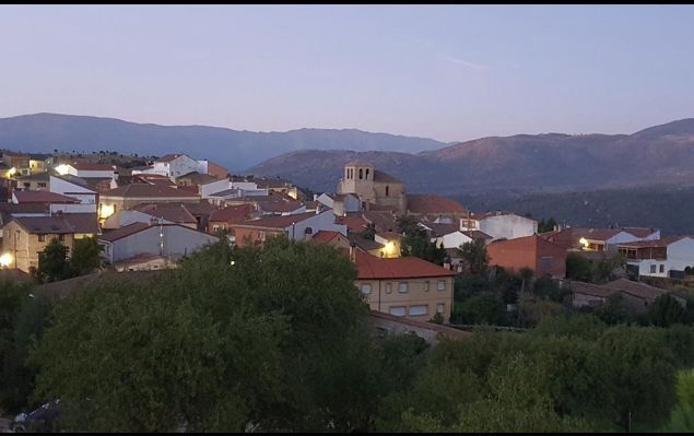 Pueblo en la ladera de una colina al atardecer, con casas de tejados rojos y montañas al fondo.
