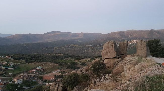 Monumento de piedra en una colina rocosa con vistas a un valle y montañas lejanas al atardecer.