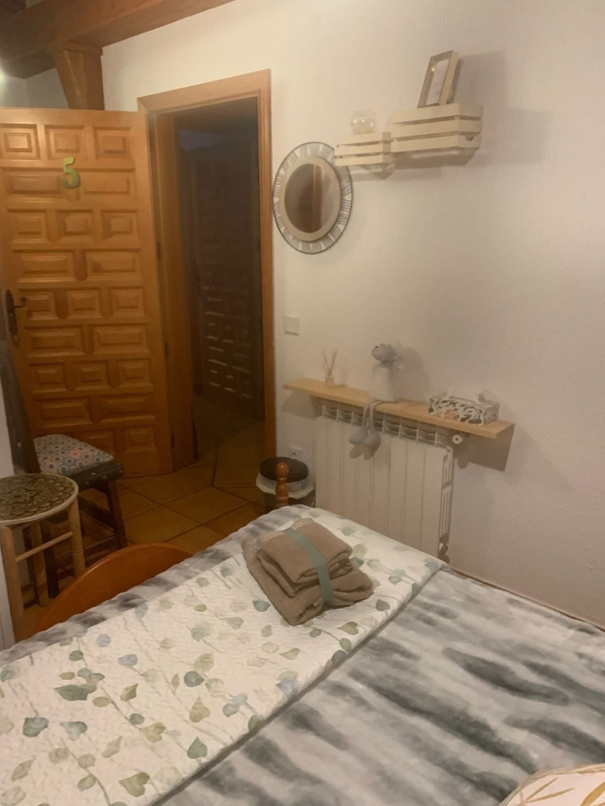 Acogedora habitación con armario de madera, estante con espejo, silla y una cama con toallas dobladas y una manta estampada.