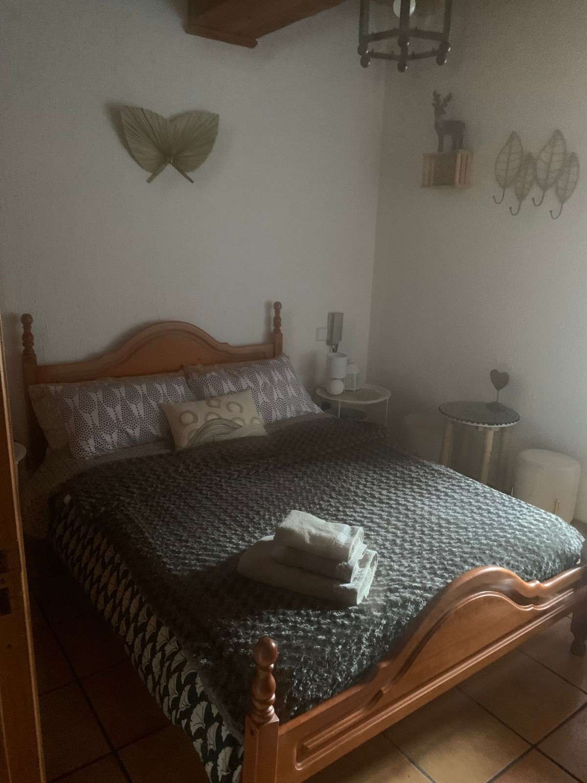Acogedora habitación con cama de madera, ropa de cama oscura con estampado y decoración de pared suave.