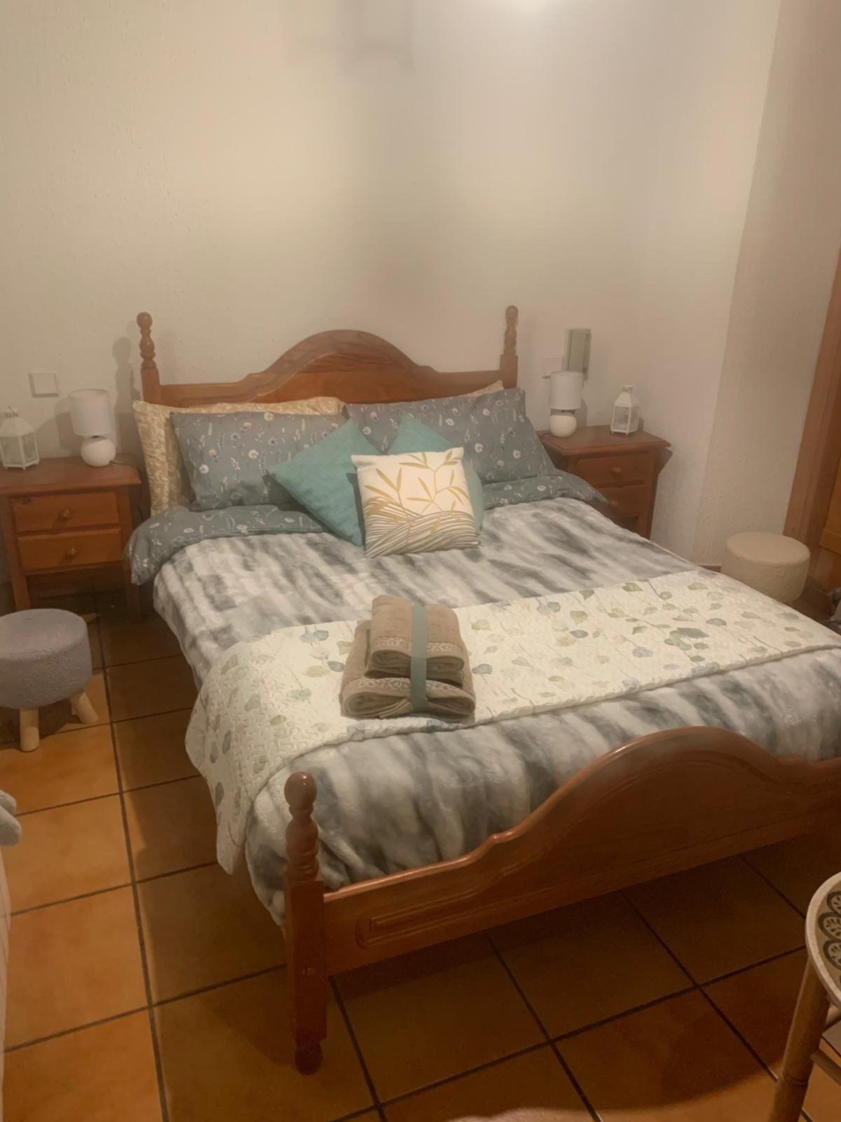Habitación acogedora con cama de madera, ropa de cama azul, mesitas de noche y suelo de baldosas de terracota.