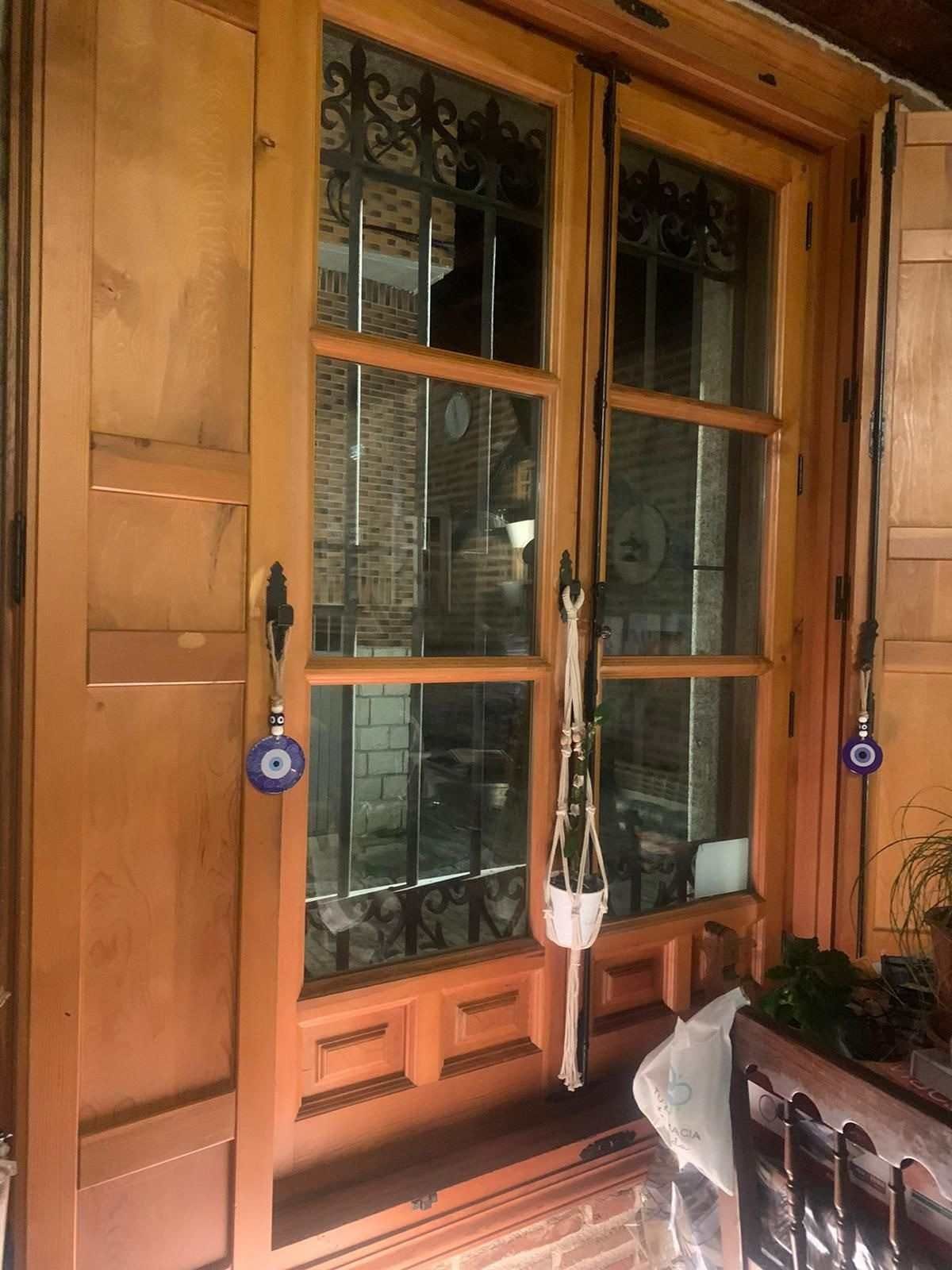 Puerta de entrada de madera con paneles de vidrio, flanqueada por adornos colgantes morados y una planta en maceta junto a una mesa.