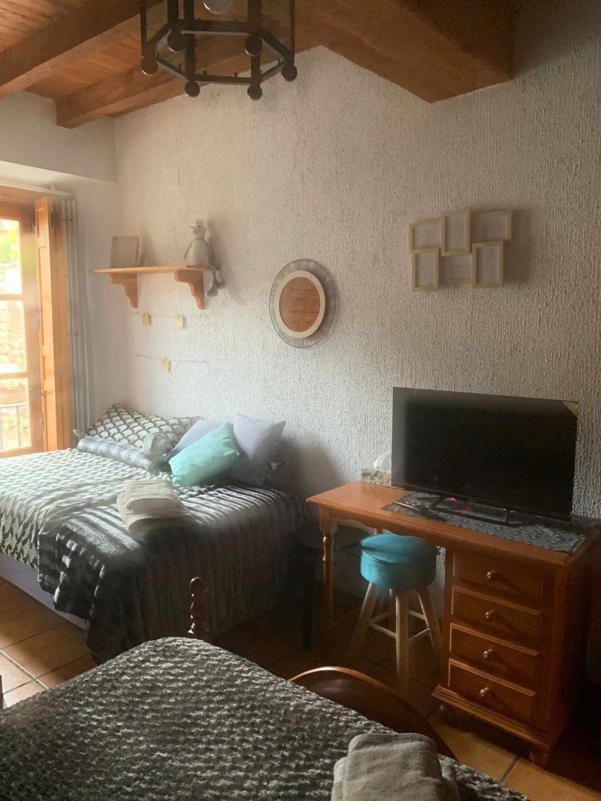 Acogedora habitación con dos camas individuales, escritorio de madera con televisión, taburete y techo con vigas vistas.
