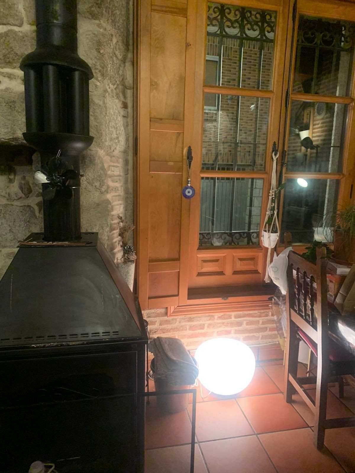 Estufa de leña junto a una puerta de madera en una habitación de piedra, con una lámpara brillante sobre el suelo de baldosas.
