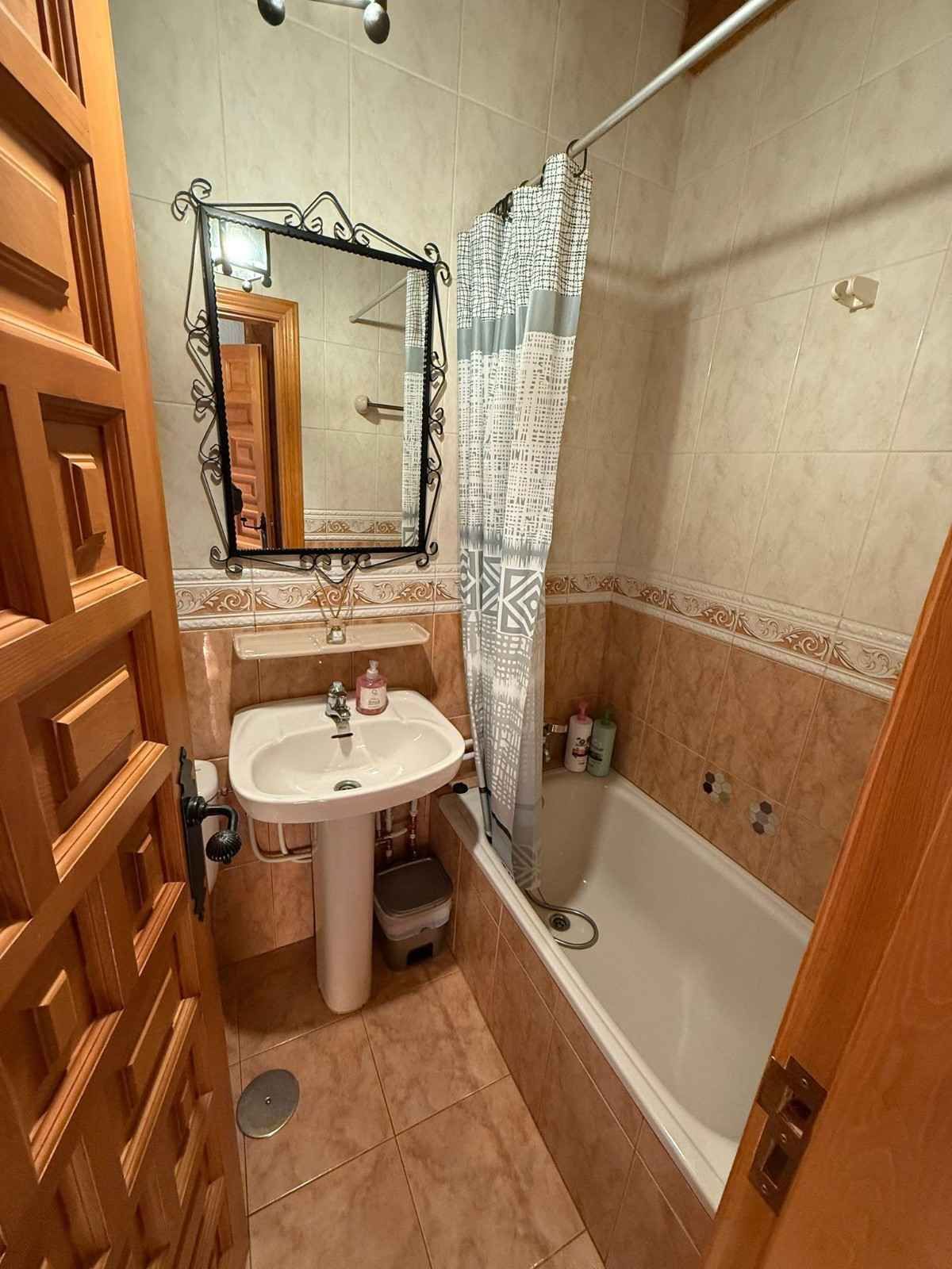Baño pequeño de color beige con lavabo, espejo, inodoro y bañera con cortina de ducha.