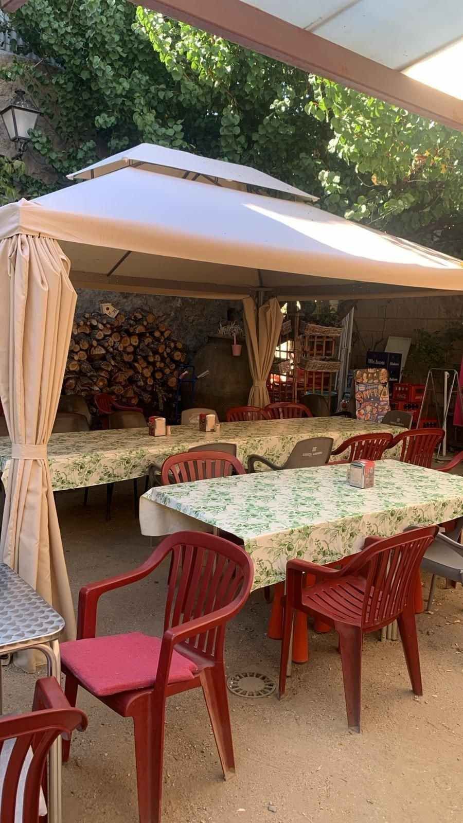 Terraza de café con sillas rojas, mesas estampadas y un gran toldo blanco bajo los árboles.