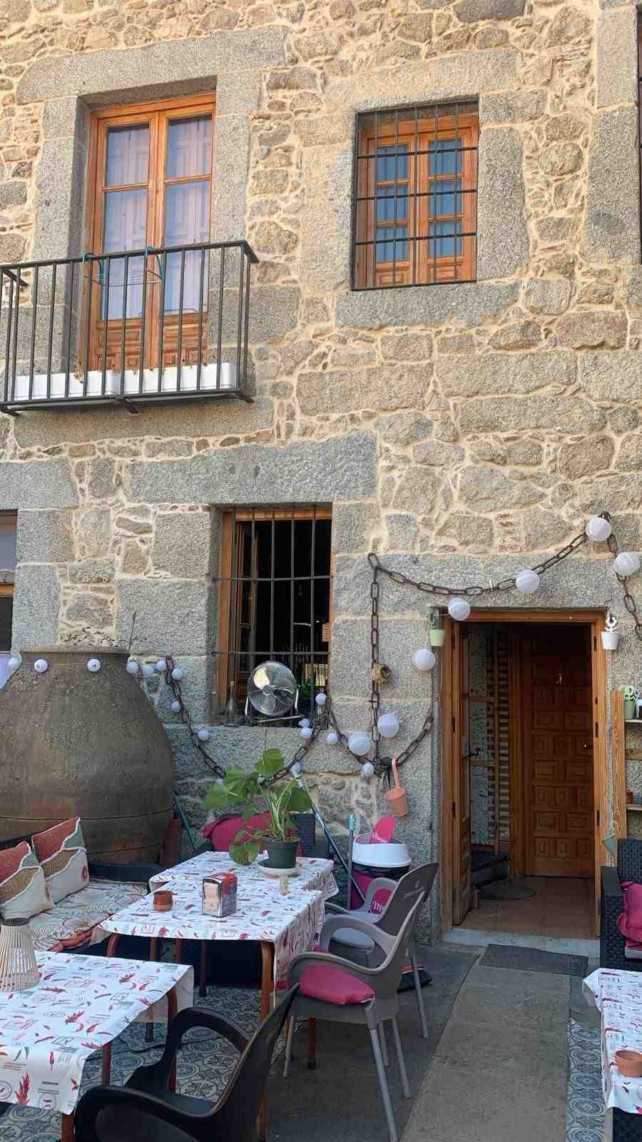 Mesas de café al aire libre junto a un edificio de piedra con ventanas y puerta de madera, vestidas con manteles a cuadros rojos y blancos.