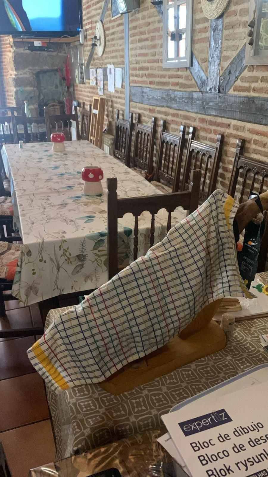 Acogedora mesa de restaurante con cojines estampados, mesa larga y paredes de ladrillo a lo largo de un estrecho pasillo de comedor.
