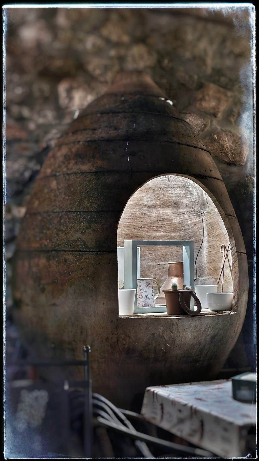 Abertura rústica de piedra arqueada con una pequeña ventana y cerámica en el interior de una habitación oscura y desgastada.