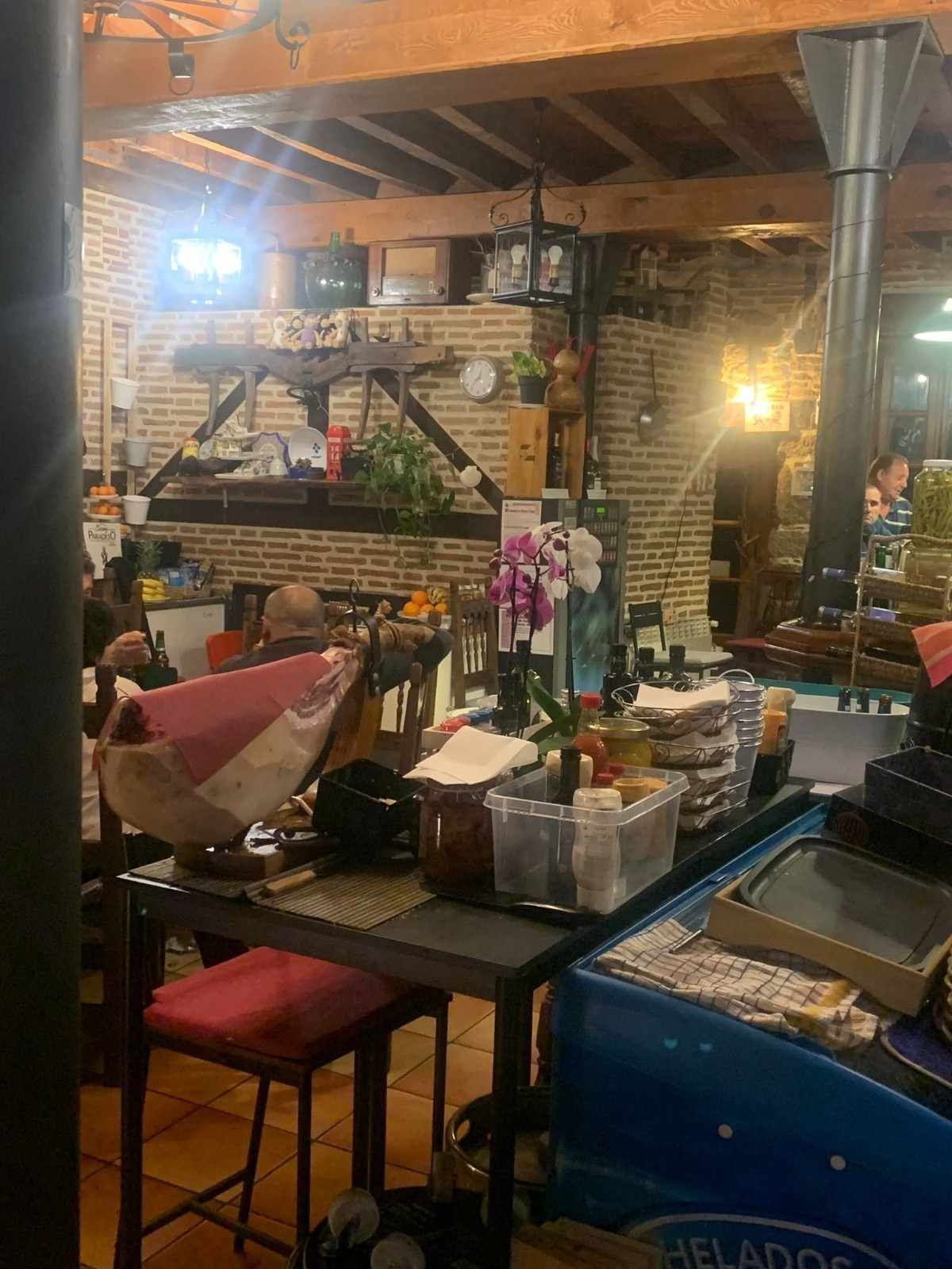 Interior acogedor de estilo rústico de cafetería con paredes de ladrillo visto, vigas de madera, mesas, sillas y cálidas lámparas colgantes.