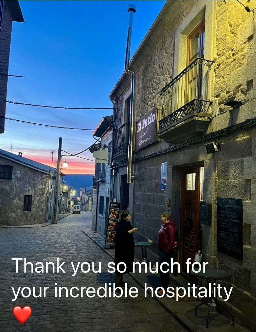 Calle empedrada antigua al atardecer con dos personas fuera de un edificio y un mensaje de texto que dice: