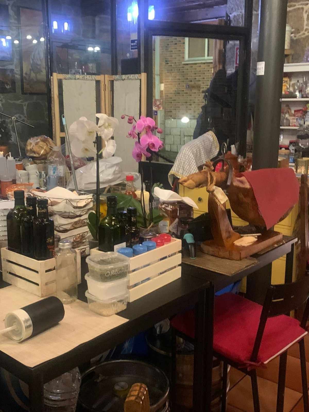 Arreglo floral sobre una mesa de café con orquídeas rosas, plantas y objetos apilados junto a una ventana.