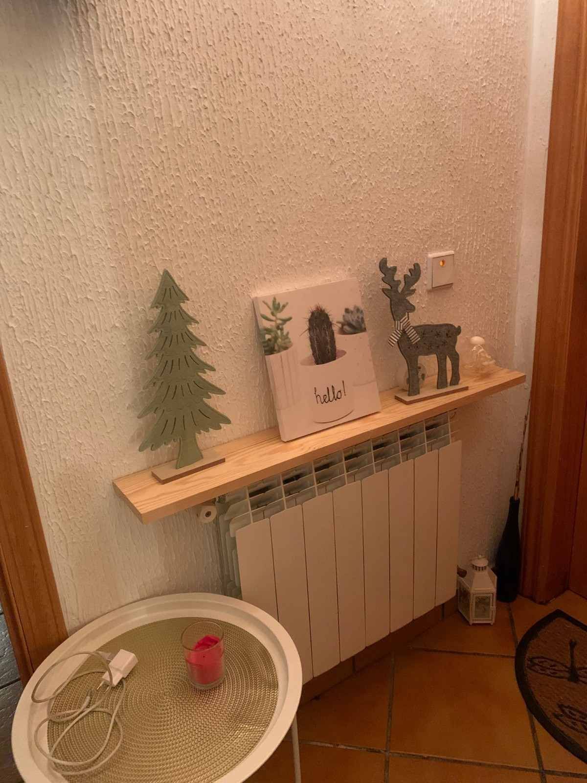 Repisa del radiador decorada con un pequeño árbol, una lámina enmarcada, una figurita de ciervo y una mesa redonda delante.