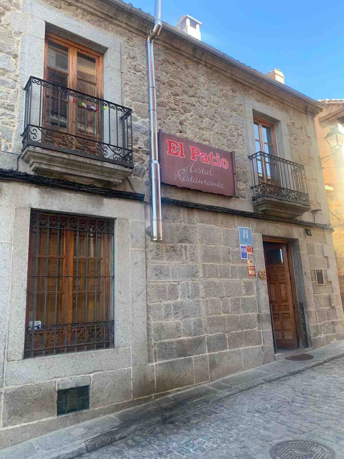 Edificio de piedra con ventanas y balcones enrejados en una estrecha calle empedrada, con un letrero rojo sobre la puerta.