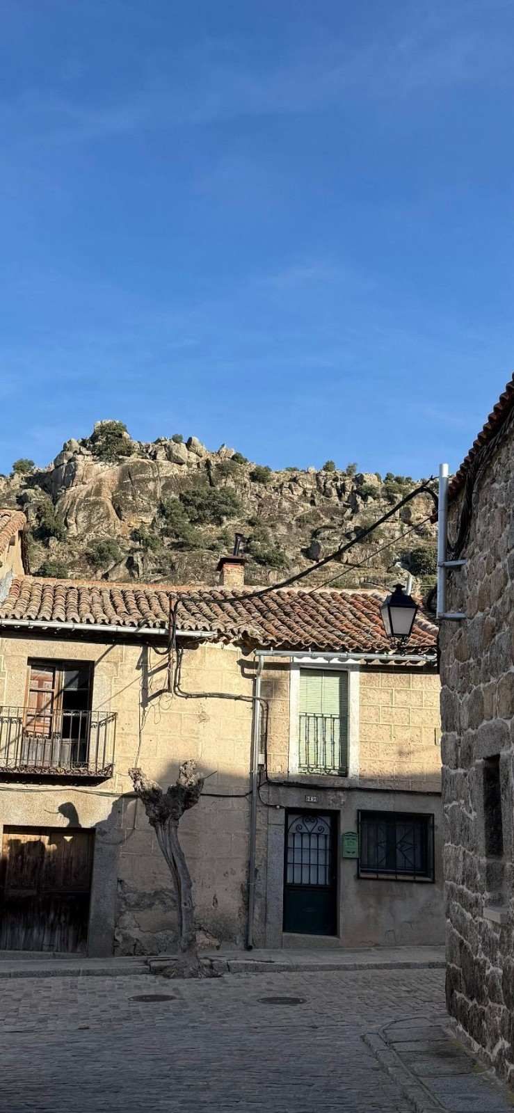 Patio de una casa de piedra bajo una ladera rocosa bajo un cielo azul