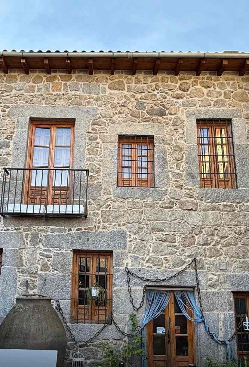 Fachada de piedra con ventanas de madera y pequeños balcones bajo un tejado de tejas.
