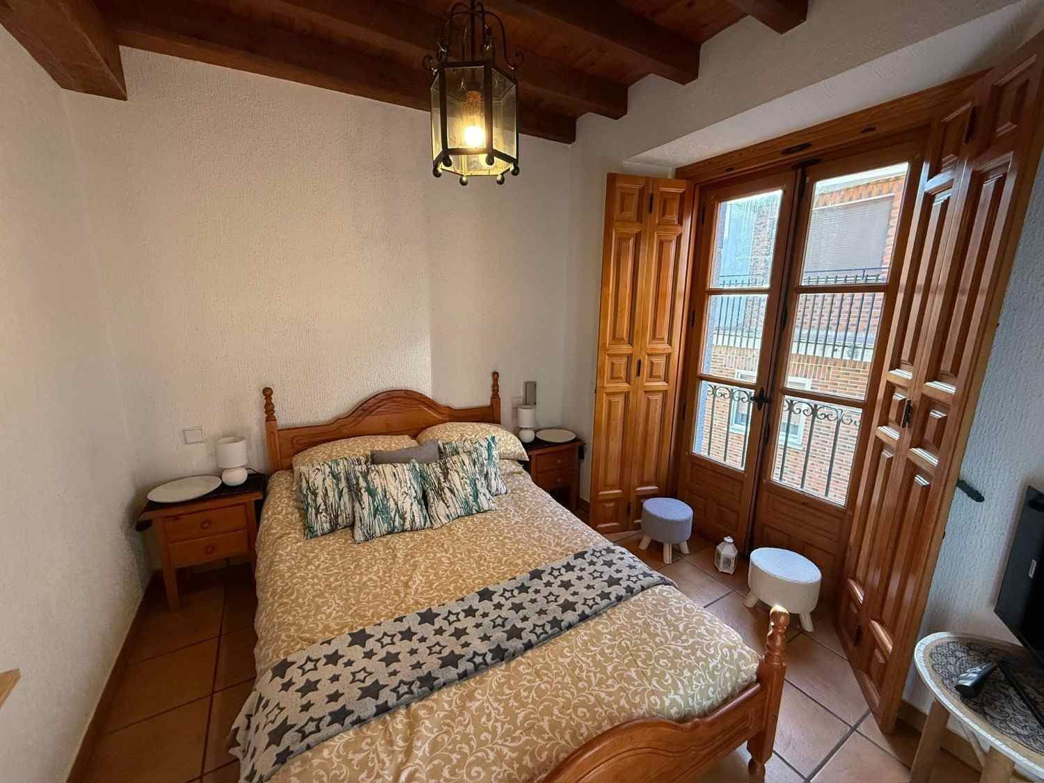 Habitación acogedora con cama, vigas de madera y puertas abiertas que dan al balcón y dejan entrar la luz natural.