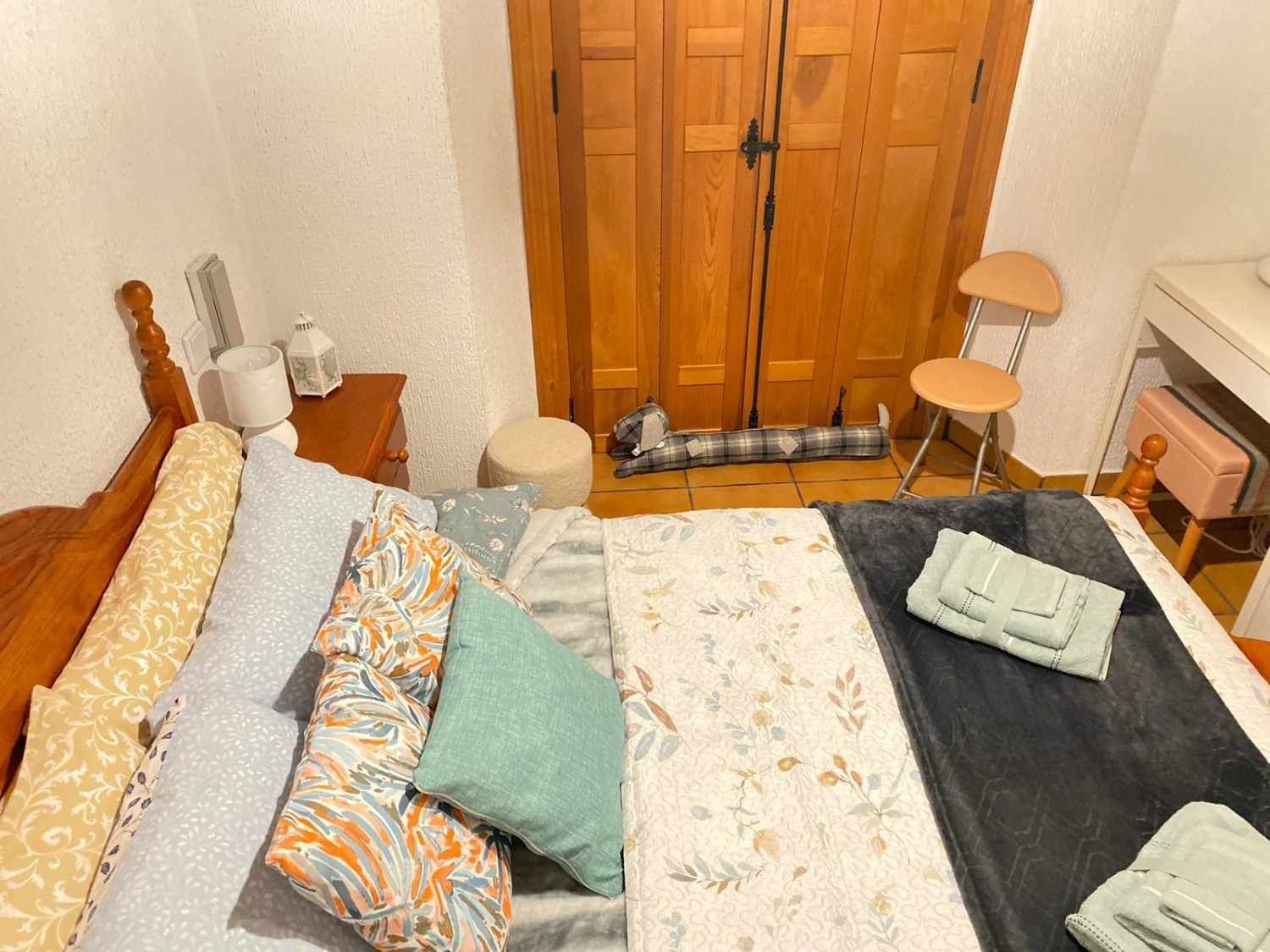 Dormitorio con cama de madera, ropa de cama estampada, toallas dobladas y puertas de madera a los pies de la cama.