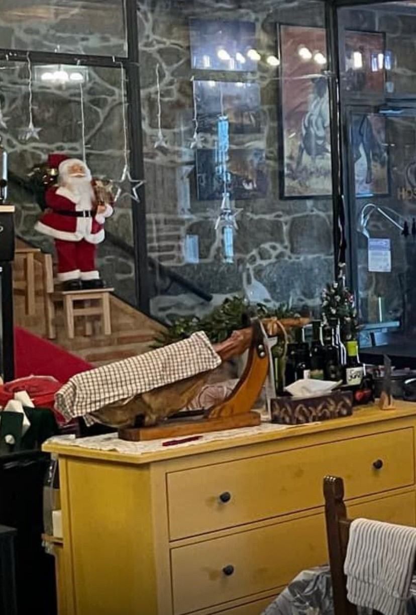 Figura de Papá Noel en una escalera junto a una cómoda amarilla, con regalos envueltos y botellas frente a unas puertas de cristal.