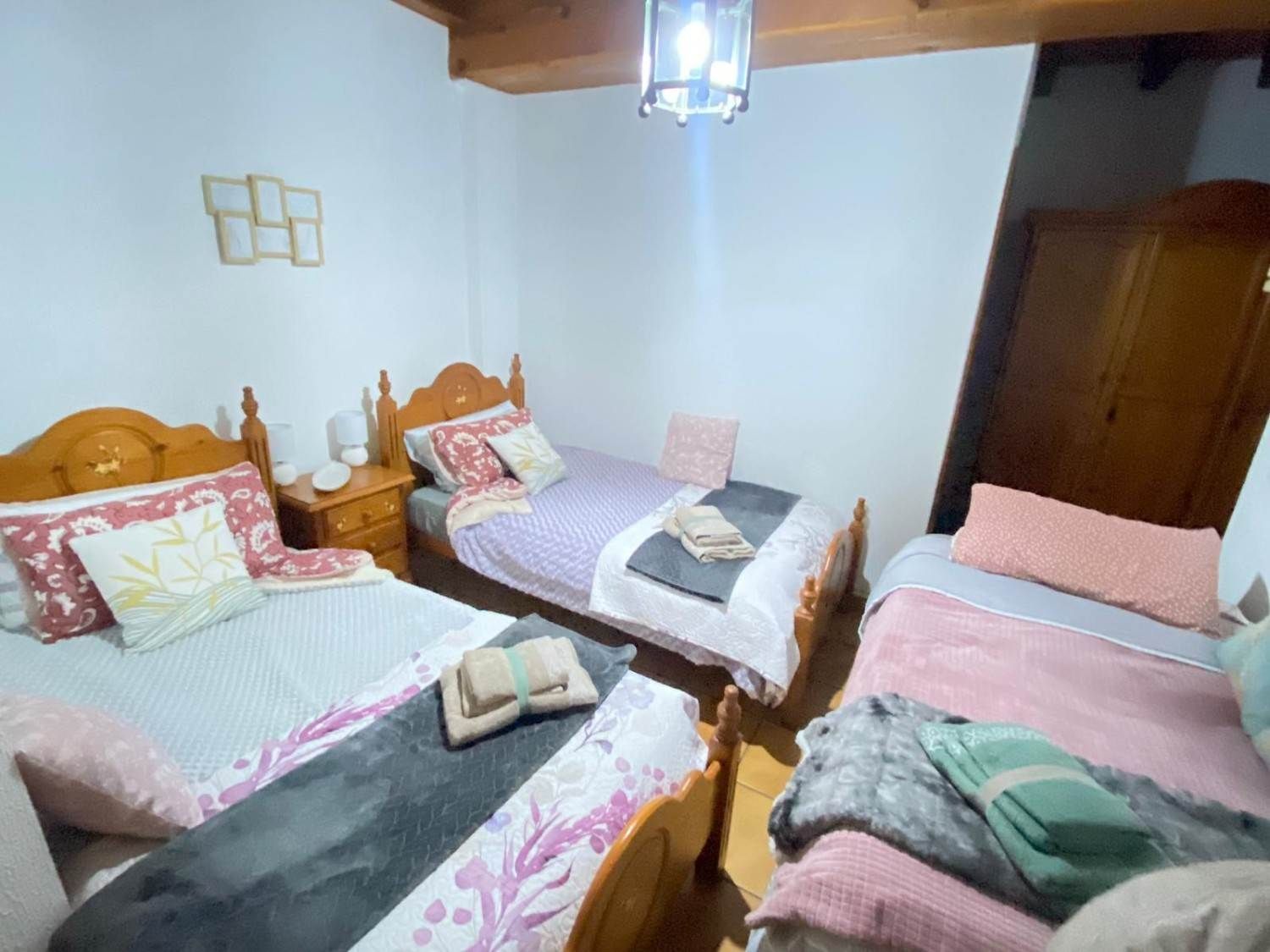 Tres camas individuales con ropa de cama en tonos pastel en una pequeña habitación con paredes blancas y muebles de madera.