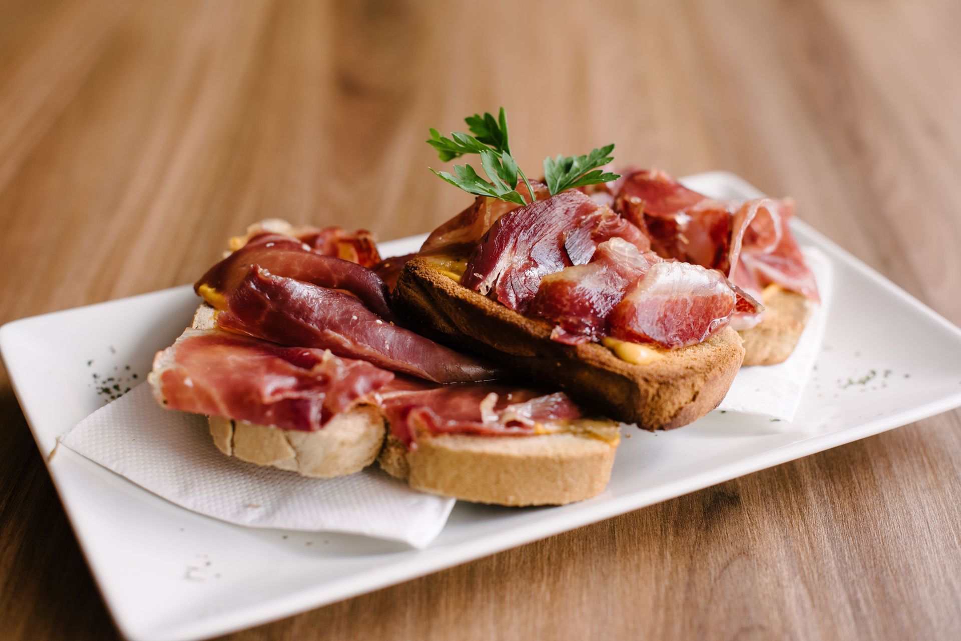 Un plato blanco cubierto con rebanadas de pan y carne sobre una mesa de madera.