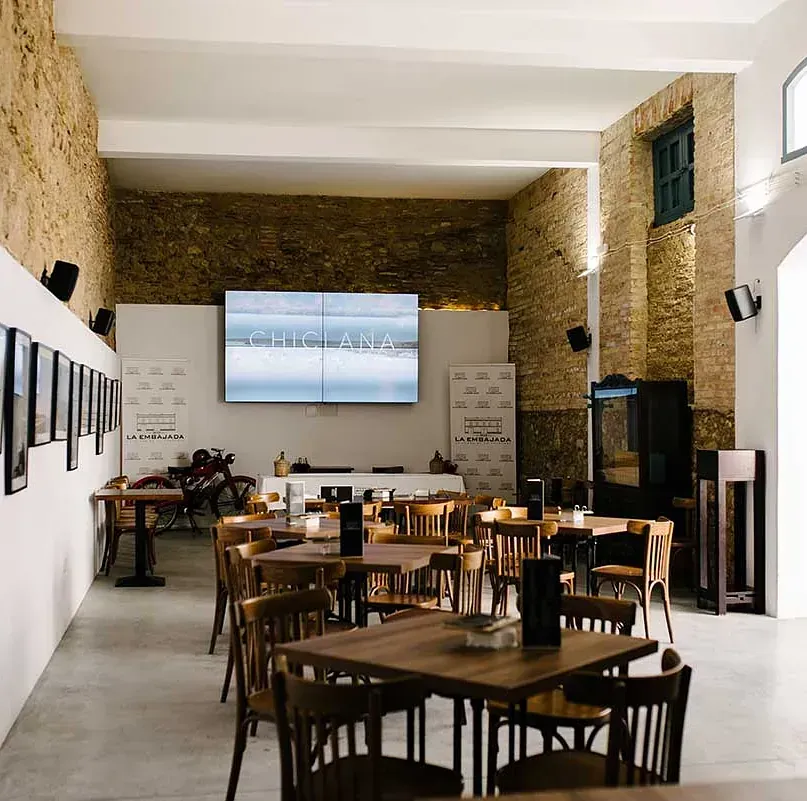 Un restaurante con mesas y sillas y una gran pantalla en la pared.