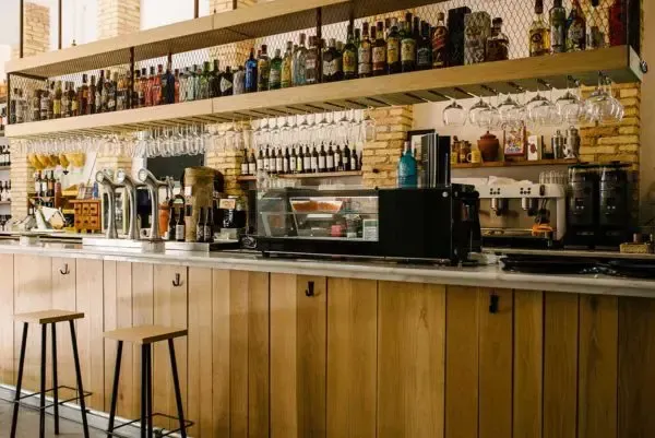 Un bar con muchas botellas en los estantes y taburetes.