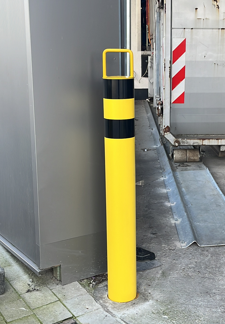 Gelber Poller mit schwarzen Streifen und quadratischer Oberseite, in der Nähe einer Laderampe.