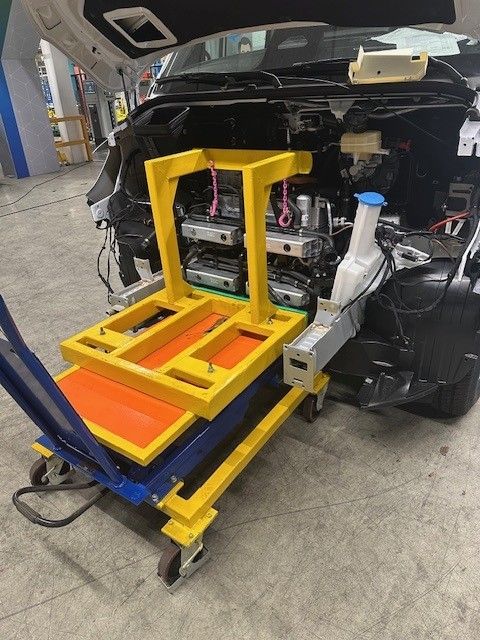 Gelber und blauer Motorstützwagen unter einem Auto in einer Reparaturwerkstatt.