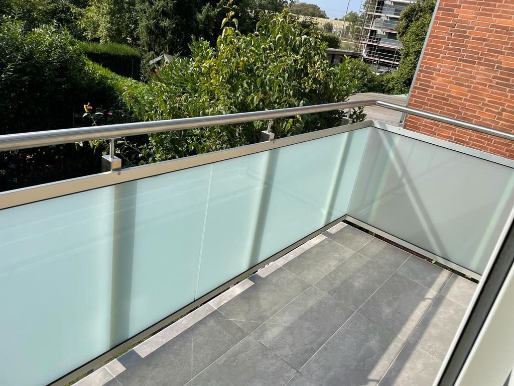 Balkon mit Milchglasplatten und Metallgeländer mit Blick auf Bäume.