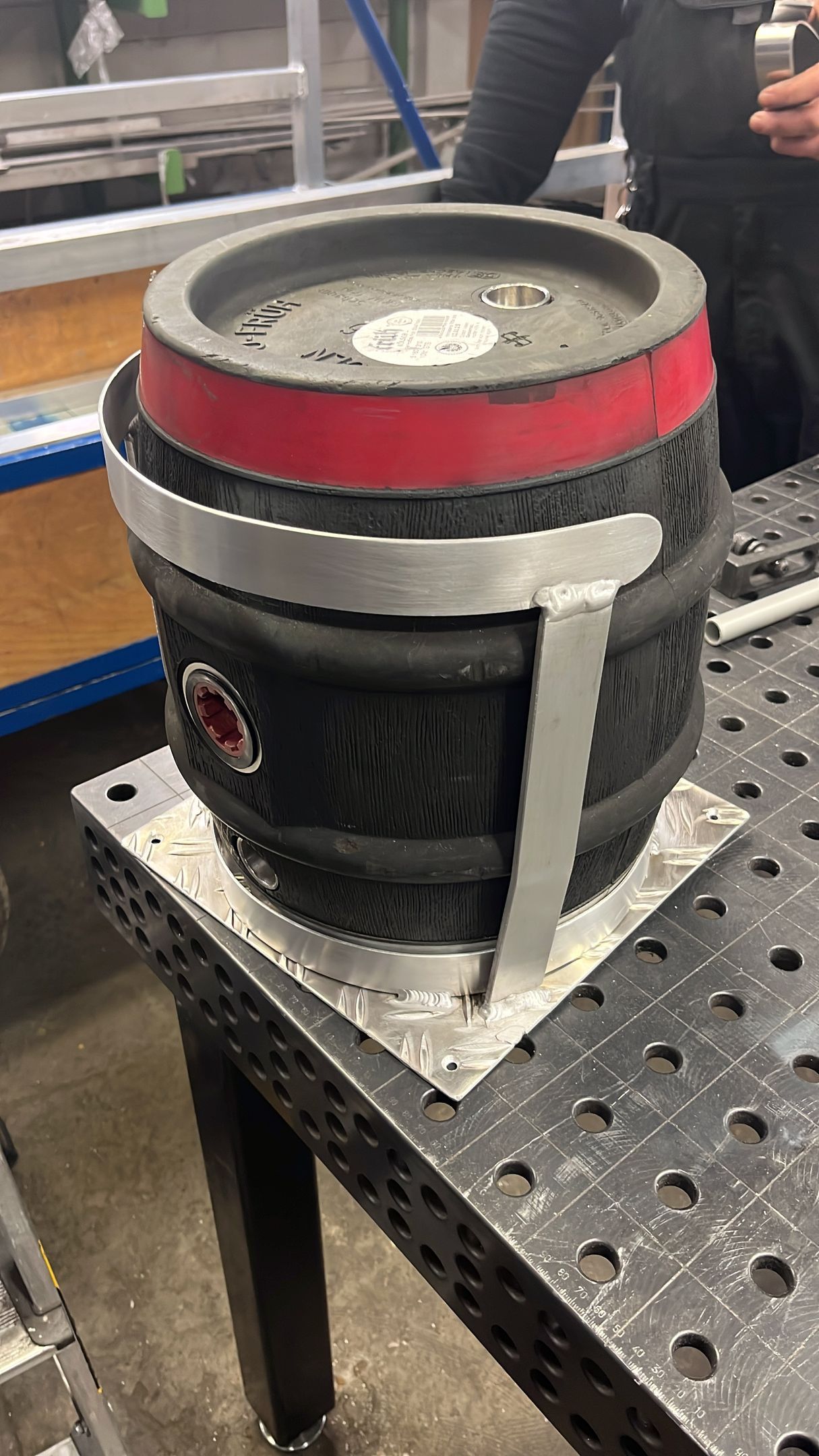 Ein kleines schwarzes Fass mit roten und silbernen Akzenten steht auf einer silbernen Metallplatte und einer Werkbank.