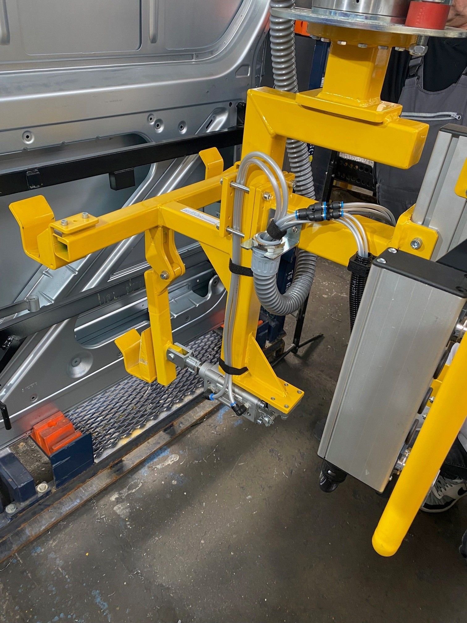 Gelbe Roboterarmvorrichtung in der Nähe eines Autorahmens in einer Werkstattumgebung.