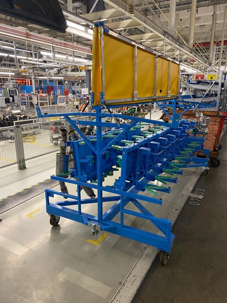 Blauer Wagen mit Komponenten beladen auf einer Fabriketage, darauf eine gelbe Struktur.