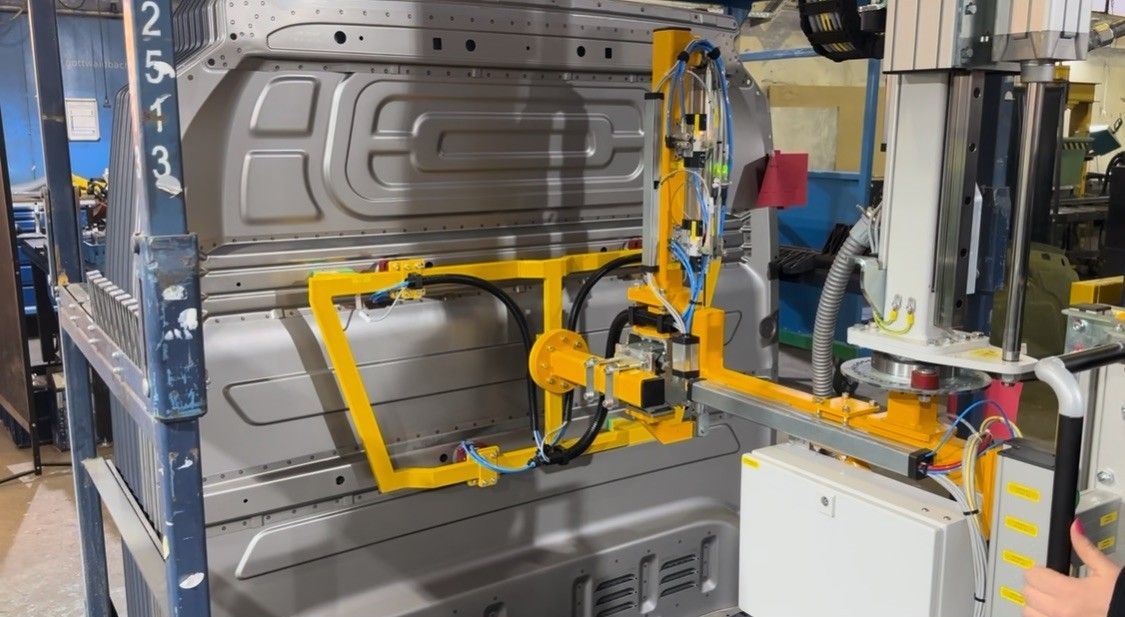 Roboterarm schweißt Fahrzeugkarosserien in einer Fabrik; gelber Arm, silbernes Metall, industrielle Umgebung.