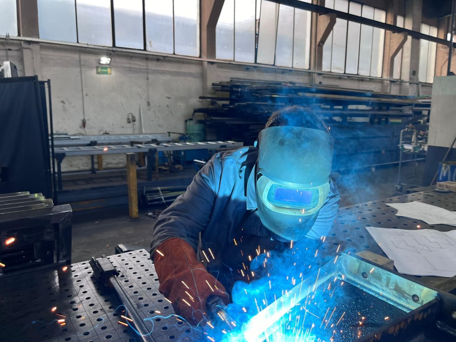 Schweißer in einer Werkstatt mit Schweißbrenner. Funken, helles Licht und Schutzausrüstung sichtbar.