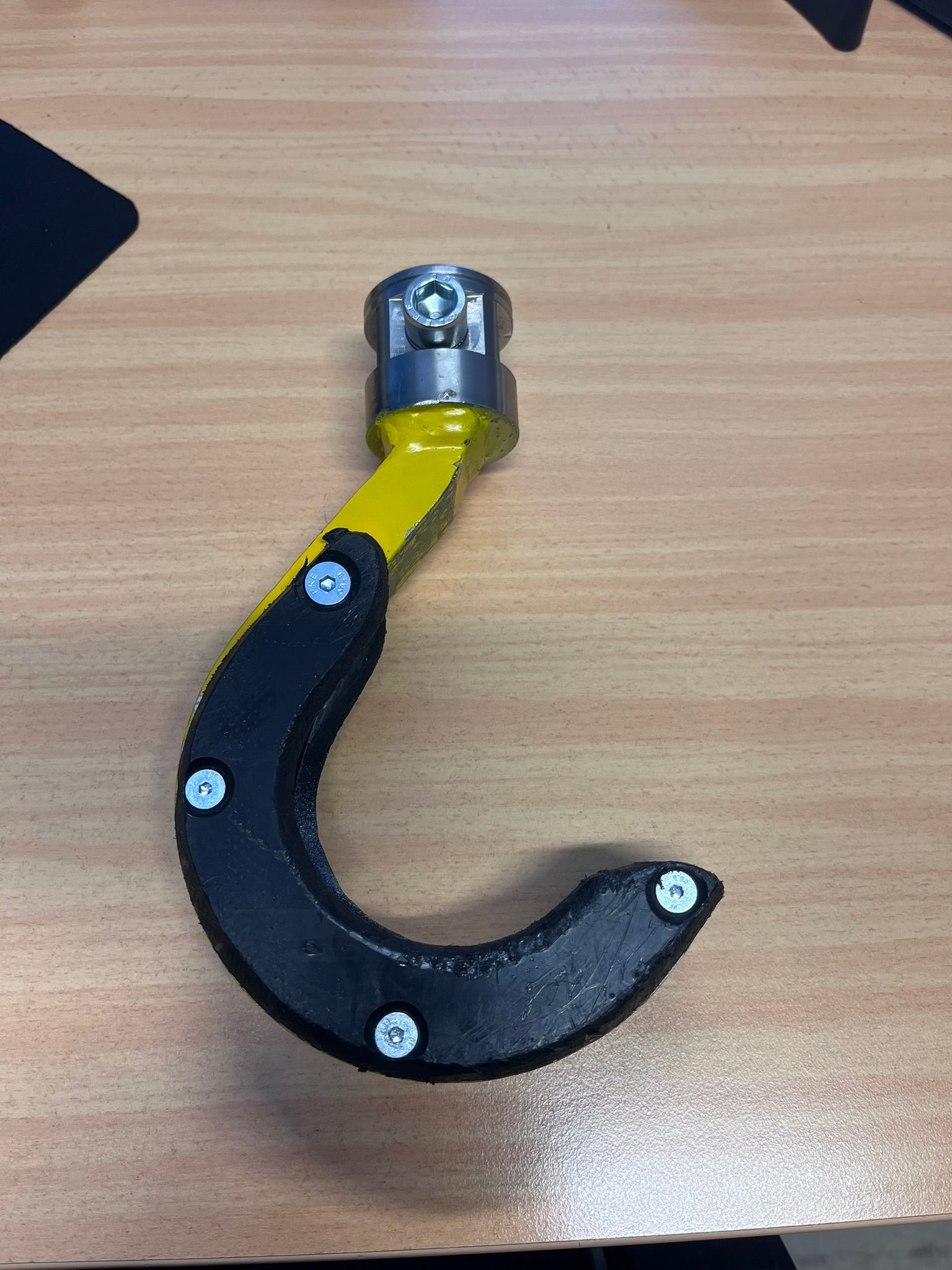 Gelber und schwarzer Industriehaken auf einer Holzoberfläche.