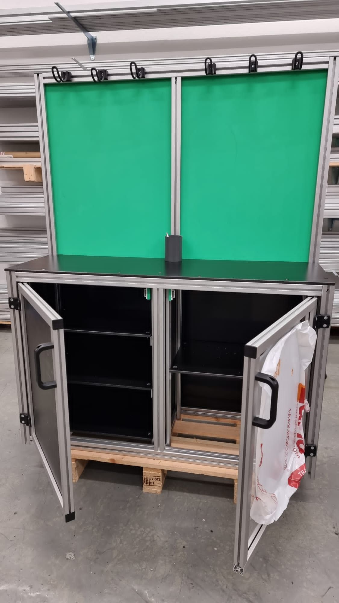 Schrank mit Aluminiumrahmen, grünen Bildschirmen, offenen Türen und einer Plastiktüte auf einer Palette.