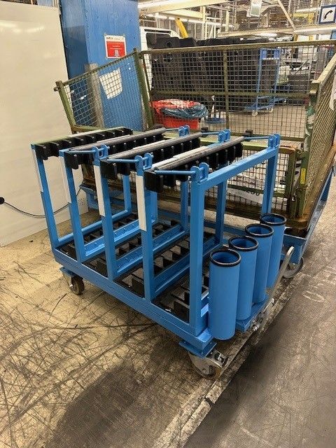 Blauer Metallwagen mit zylindrischen Behältern und Haltegestellen, wahrscheinlich für Industrieteile.