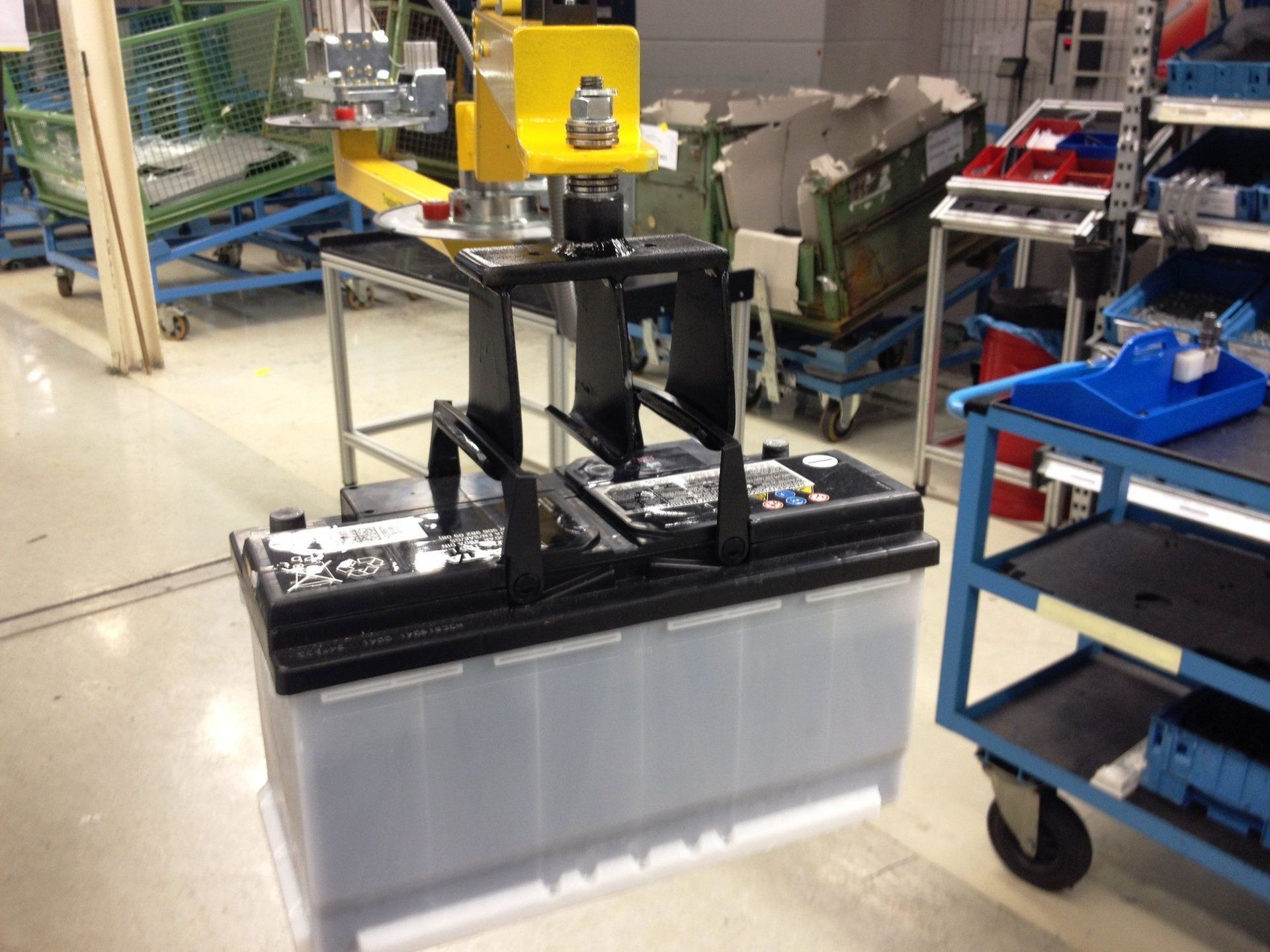 Eine große Industriebatterie befindet sich unter einem gelben Hebemechanismus in einer Fabrik.