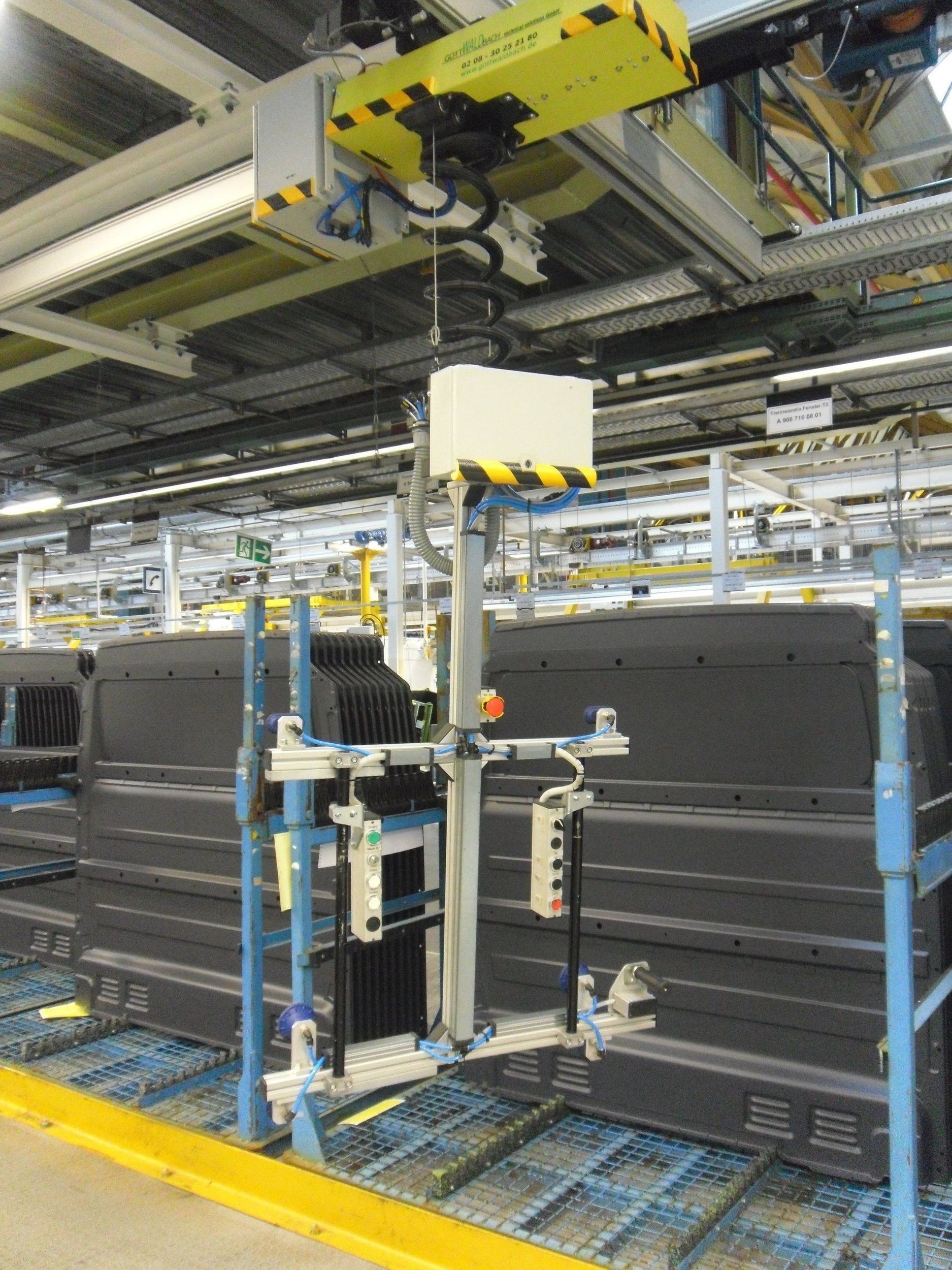 Automatisiertes Fließband in einer Fabrik mit einem hängenden Roboterarm über dunklen Behältern auf einem Förderband.