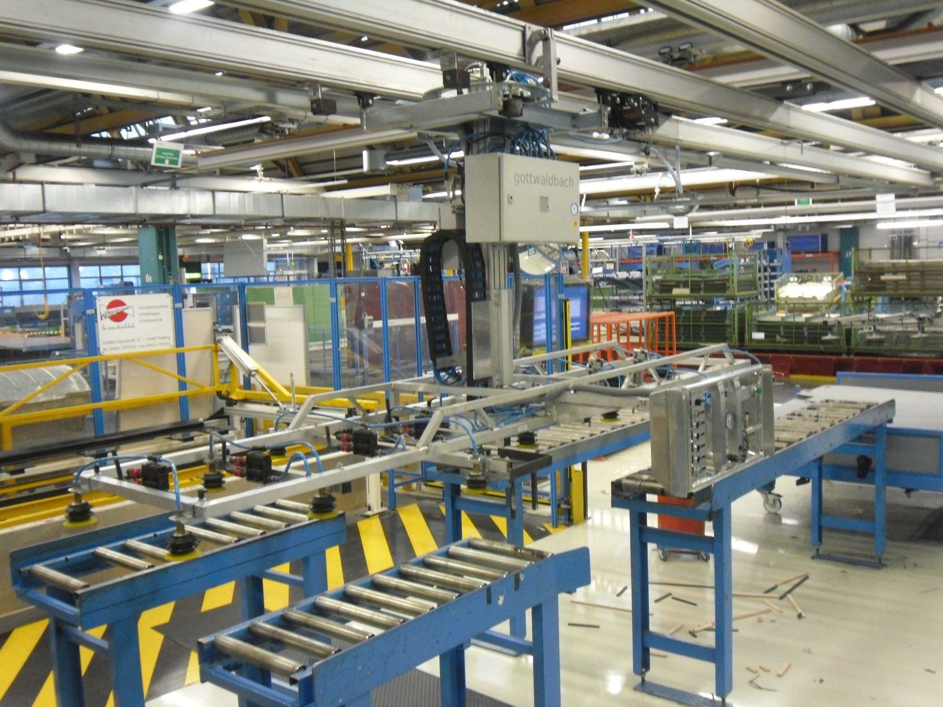 Fließband in einer Fabrik mit einem Roboterarm, der einen Metallrahmen zwischen Förderbändern anhebt.