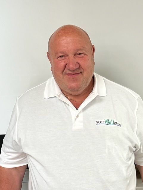 Glatzköpfiger Mann im weißen Poloshirt lächelt drinnen. Logo auf dem Shirt: „Gotts Will Change.“