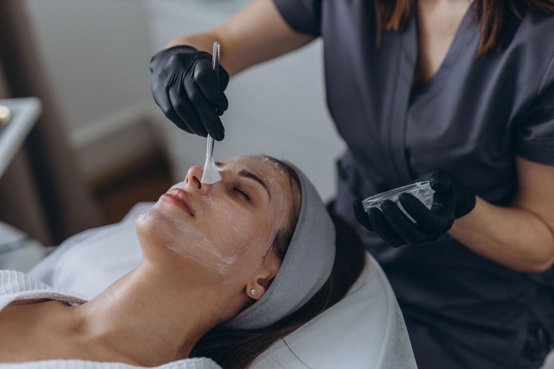 Esteticista con guantes aplica un tratamiento facial a una mujer tumbada en una camilla de spa.