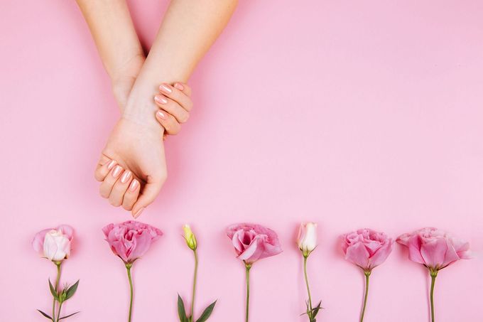 Dos manos entrelazadas sobre flores rosas sobre un fondo rosa pastel.