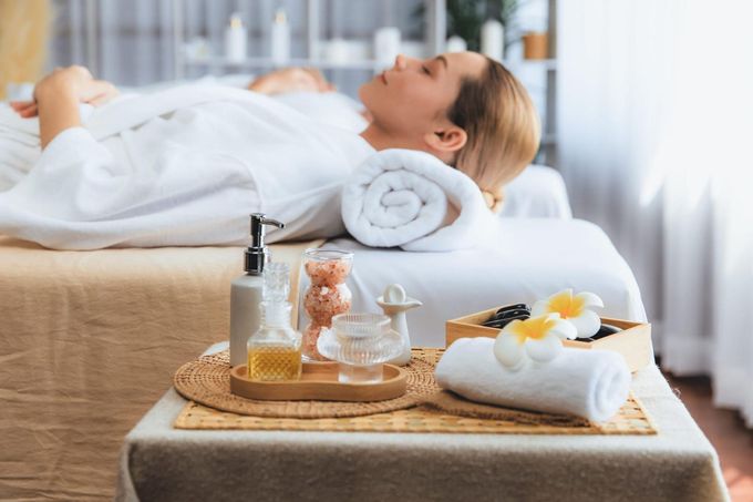Una persona tumbada en una camilla de spa con toallas enrolladas y aceites de masaje en una bandeja cercana.